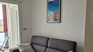 Un divano grigio con due cuscini, un quadro incorniciato che raffigura un panorama urbano e una lampada a soffitto in fibra naturale.