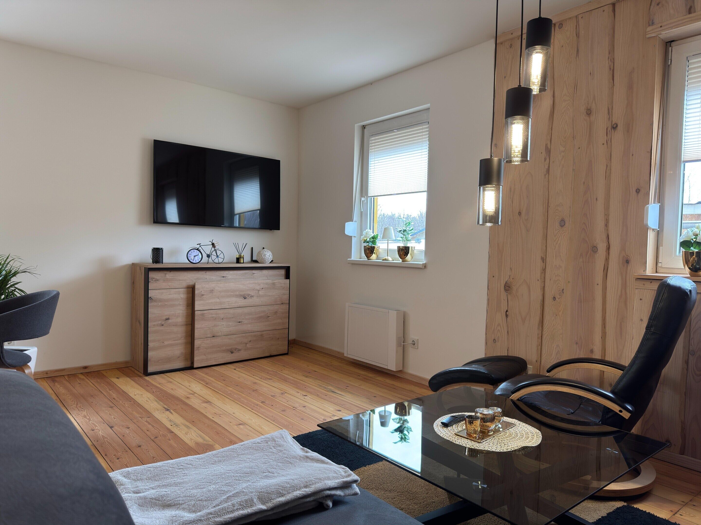 A modern living room with a glass coffee table, a sofa, a TV mounted on the wall, and a wooden cabinet.