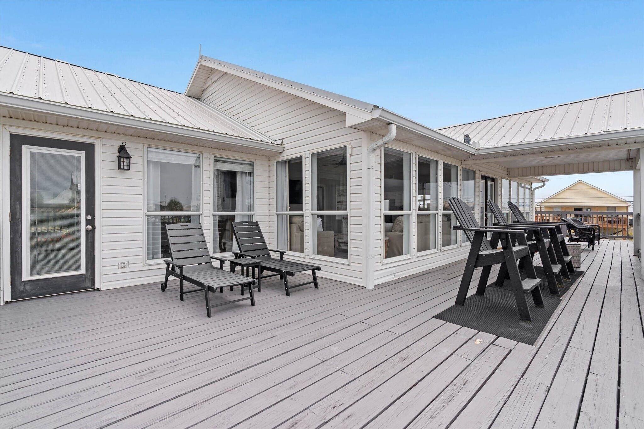 A covered outdoor deck with multiple lounge chairs and a table, a white building with large windows, and a clear sky.