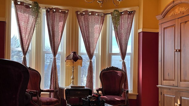 A room with a corner window, a wooden cabinet, two armchairs, a table, and a lamp.