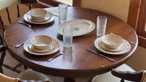 A round wooden dining table with white plates, bowls, and cutlery, set for four.