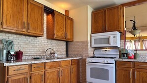 A kitchen with wooden cabinets, a white stove, a microwave, and a sink.