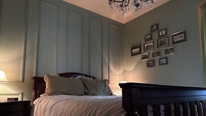 A bedroom with a bed, a nightstand, a dresser, a chandelier, and framed pictures on the wall.