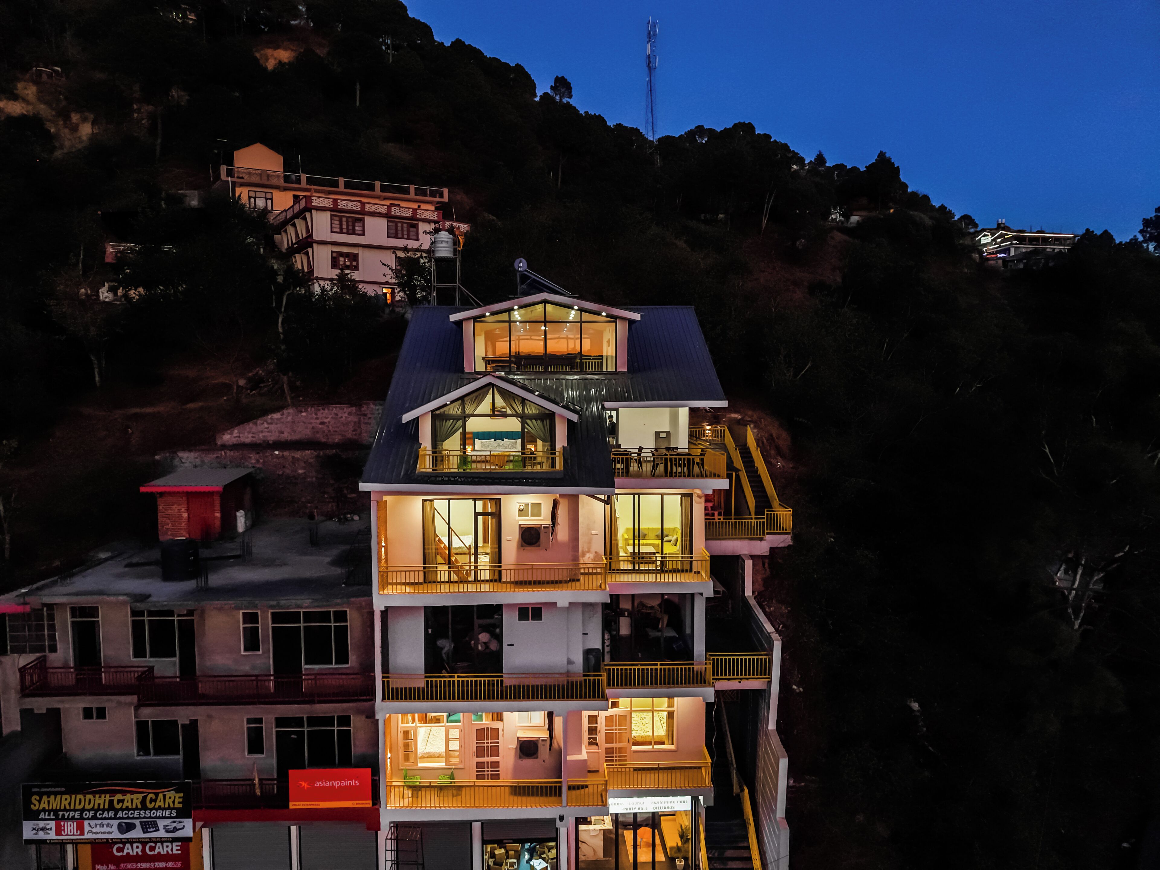 Un edificio de varios pisos con balcones y ventanas amplias, ubicado en una ladera con otros edificios al fondo.