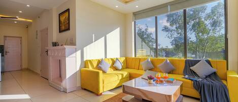 A modern living room with a yellow sofa, a coffee table, and a large window with a view of trees.