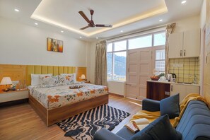 A bedroom with a wooden bed, a ceiling fan, a nightstand, a bedside table, a sofa, a window with curtains, and a view of the outdoors. - Hillshades Retreat by Alaya Stays 6BHK (Solan)