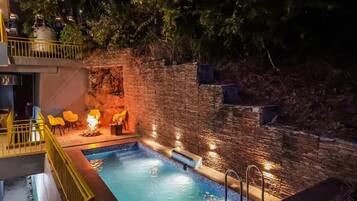 A swimming pool with a stone wall and a small fire feature.