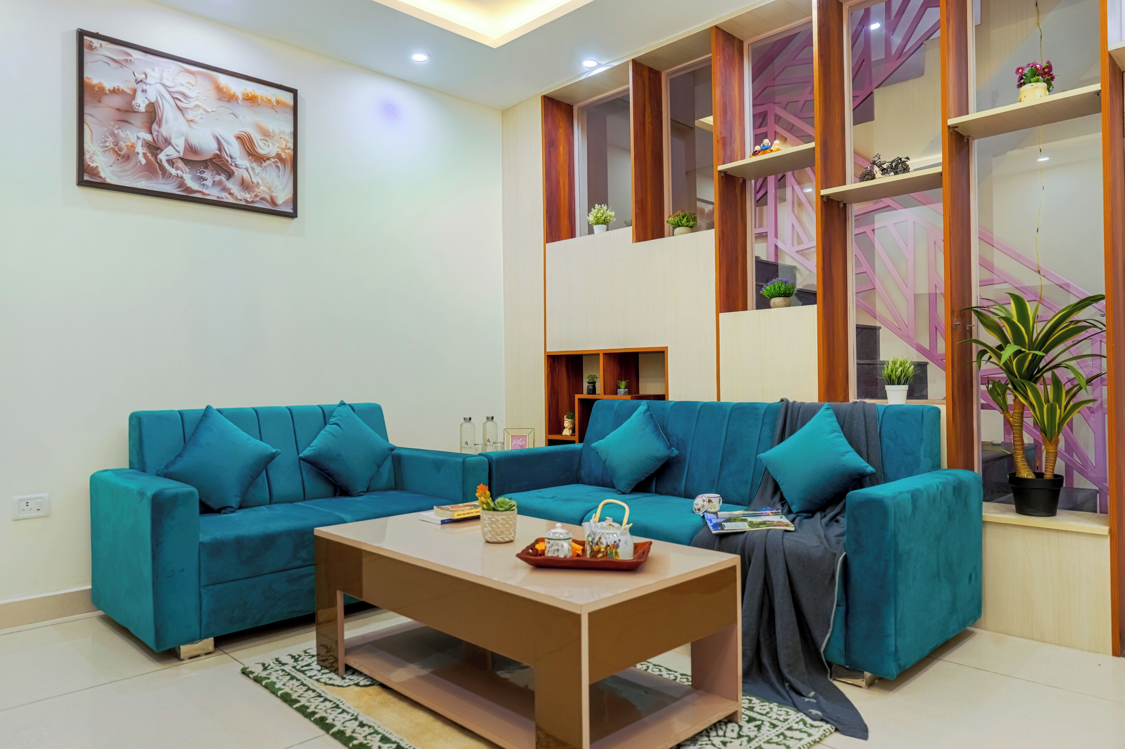 A modern living room with teal sofas, a wooden coffee table, and a large painting on the wall.