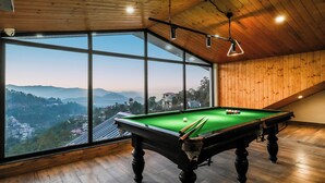 Een pooltafel met vrij uitzicht op een bergachtig landschap door grote ramen.
