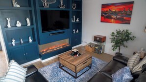 Ein modernes Wohnzimmer mit Kamin, Flachbildfernseher und Dekorationen auf Regalen.