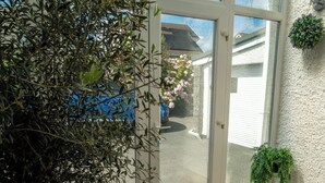 Ein Wintergarten mit einem Blumentopf-Olivenbaum, einer Fußmatte, einem Teppich und einer kleinen Pflanze an der Wand.