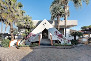 Un edificio con una entrada triangular distintiva, palmeras y un camino de ladrillo.