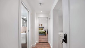 En hall som leder till ett sovrum med tvättmaskin, ett badrum med handfat och en dörr med ett modernt lås.