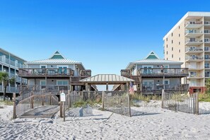 Ein Strandhotel mit mehreren Balkonen, einem überdachten Gang und einem Sandstrand.