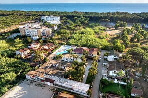 Vue aérienne d’un quartier résidentiel situé sur la côte, avec des bâtiments, une piscine et une plage.