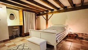 Une chambre à coucher comprenant un lit, un petit tabouret, un banc, une table de chevet avec une lampe et une fenêtre avec des rideaux.