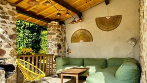 Un espace extérieur aménagé, abrité et doté d’un mur en pierre, d’un canapé vert, d’une table en bois et de luminaires suspendus.
