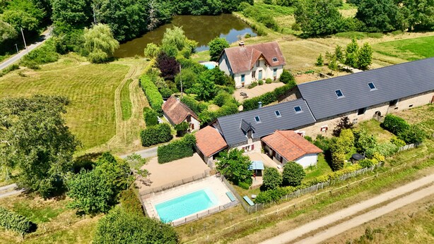 Un grand bâtiment doté de plusieurs toits, d’une piscine et d’un étang.