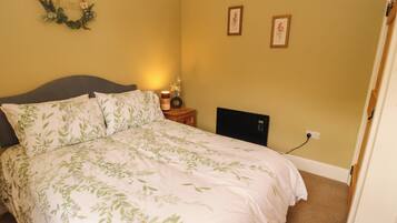 Quarto com cama, mesa de cabeceira, luminária fixada na parede e duas fotos emolduradas.