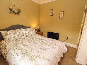 A bedroom with a bed, a nightstand, a wall-mounted light, and two framed pictures.