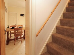 A staircase with carpeted steps leading to a landing, a wooden dining table with chairs, and a white door.
