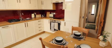 A compact kitchen with white cabinets, a dining table set for two, and a visible oven.