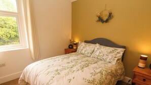 Et soveværelse med seng, natbord, lampe og et billedværk på væggen.