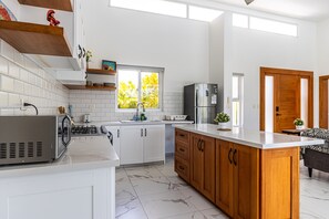 A modern kitchen with white cabinets, a wooden island, a stainless steel refrigerator, and a window with a view of greenery. - Luxurious Villa With Private Pool in Sosua (Sosúa)