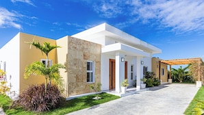 A modern two-story house with a covered patio, a well-maintained lawn, and a clear blue sky. - Family Villa With Private Pool in Sosua Ocean Village (Sosúa)