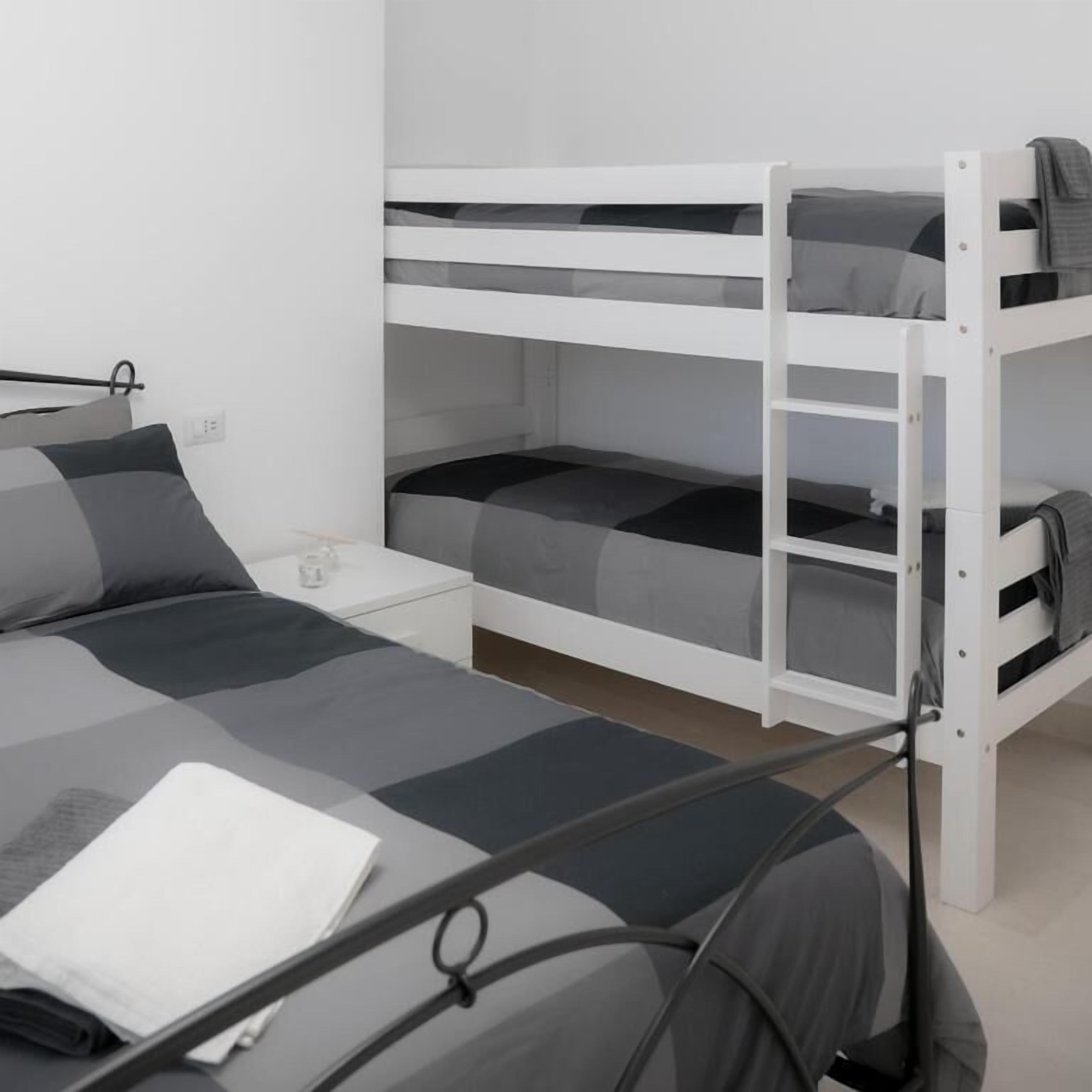 Un letto a castello con un letto inferiore, un comodino con una lampada, e un letto con un cuscino e un oggetto bianco piegato.