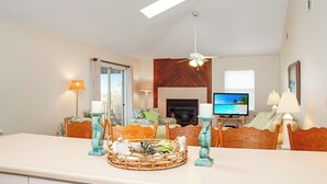 Een woonkamer met een televisie, een open haard en een eethoek met een tafel en stoelen.