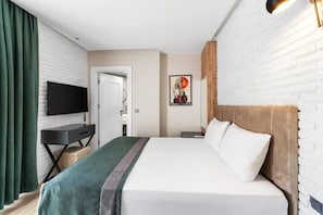 A hotel room with a bed, a desk, a TV, a painting, and a brick wall. - Nivasole Lara (Antalya)