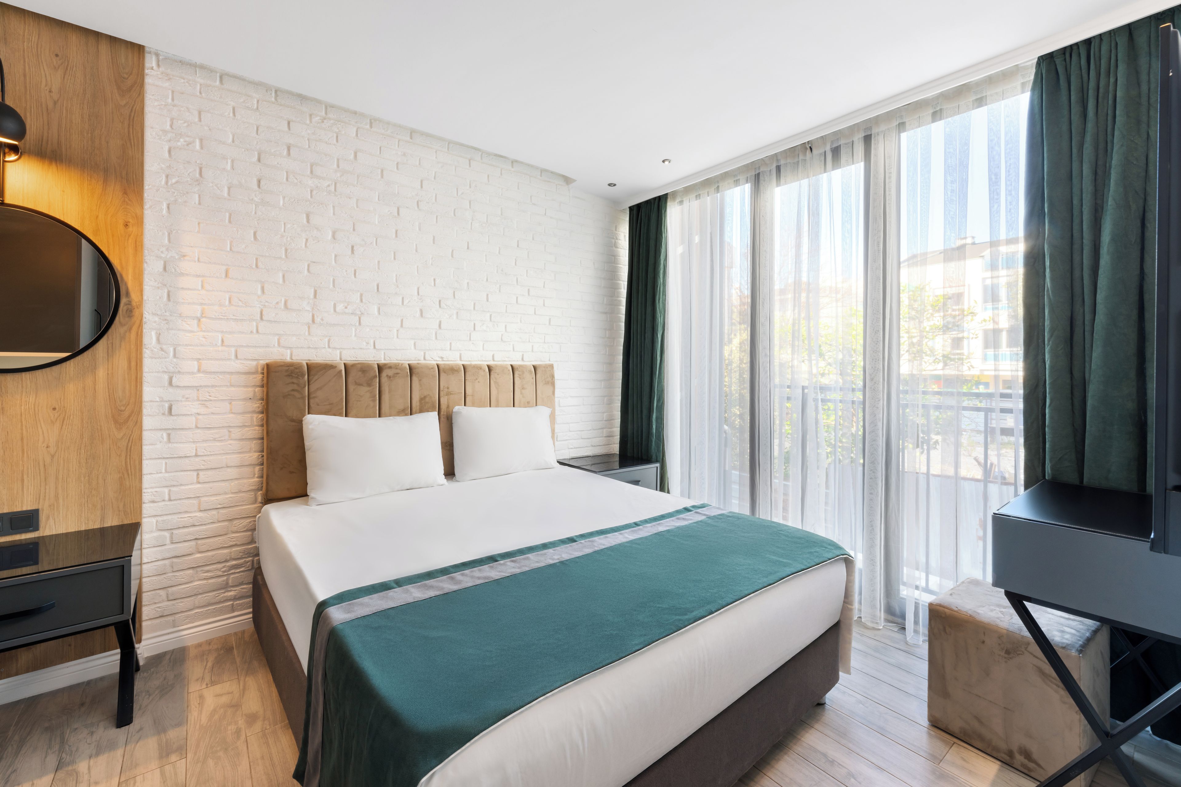 Une chambre d’hôtel avec un mur en briques, un lit recouvert d’une courtepointe verte, une télévision et une fenêtre avec des rideaux.