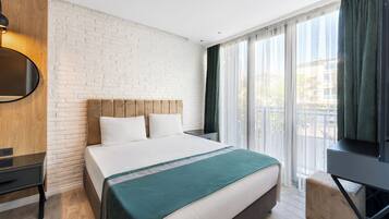 Une chambre d’hôtel avec un mur en briques, un lit recouvert d’une courtepointe verte, une télévision et une fenêtre avec des rideaux.