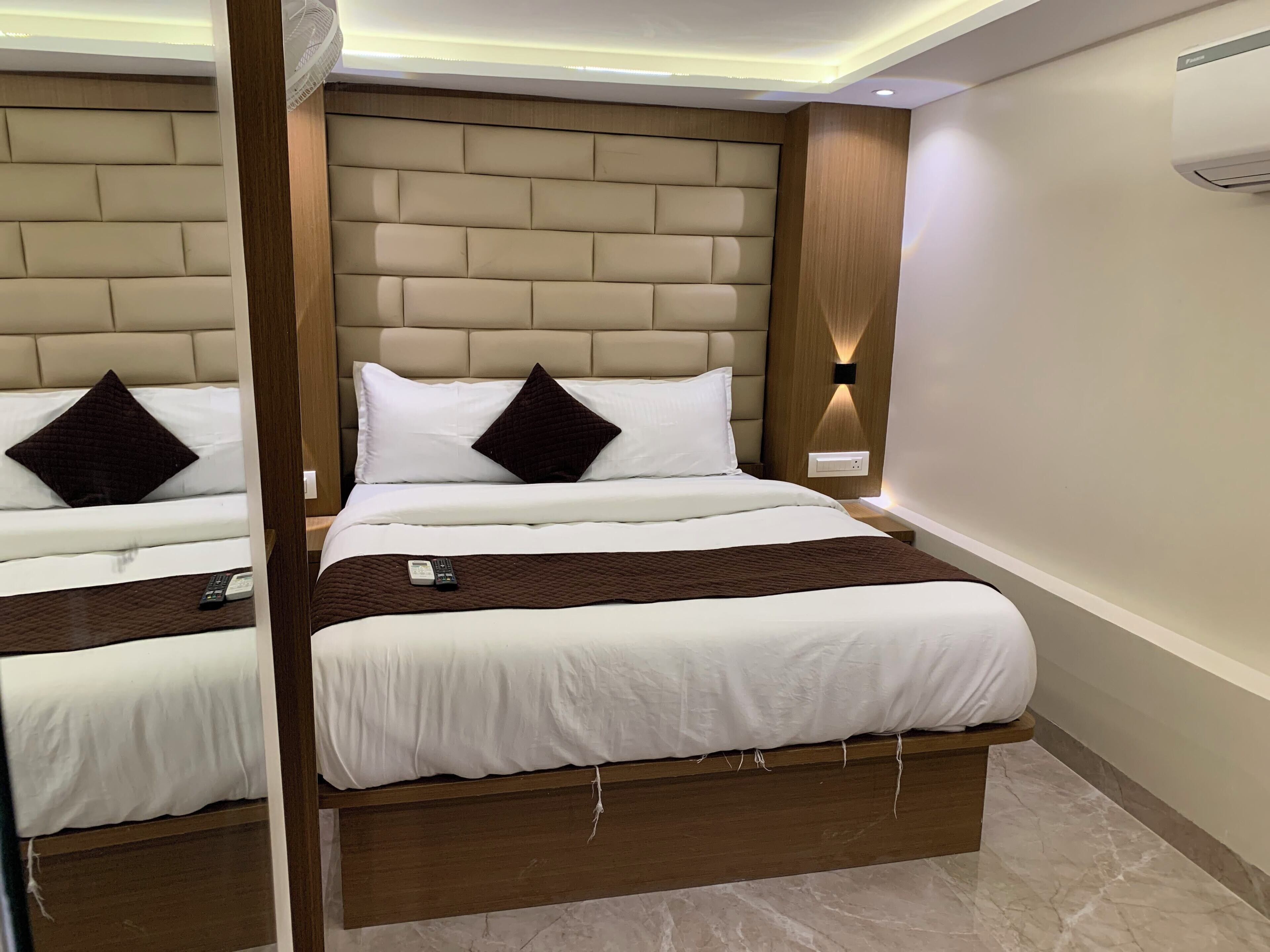A hotel room with a large bed, a bedside table, a remote control, and a wall-mounted air conditioning unit.