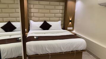 A hotel room with a large bed, a bedside table, a remote control, and a wall-mounted air conditioning unit.
