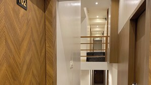 Un pasillo con puerta de madera marcada '102', diseño interior moderno y una escalera que conduce a un nivel superior.