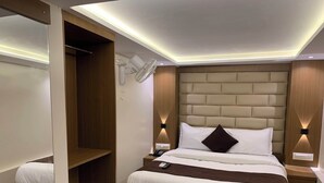 Una habitación de hotel moderna con una cama, mesitas de noche, un archivador y un ventilador de pared, además de un estante empotrado.