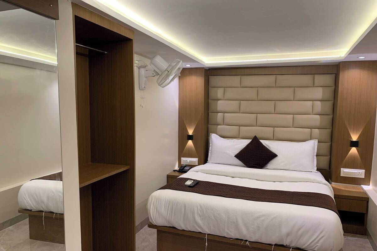 A modern hotel room with a bed, bedside tables, a nightstand, a wall-mounted fan, and a built-in shelf.