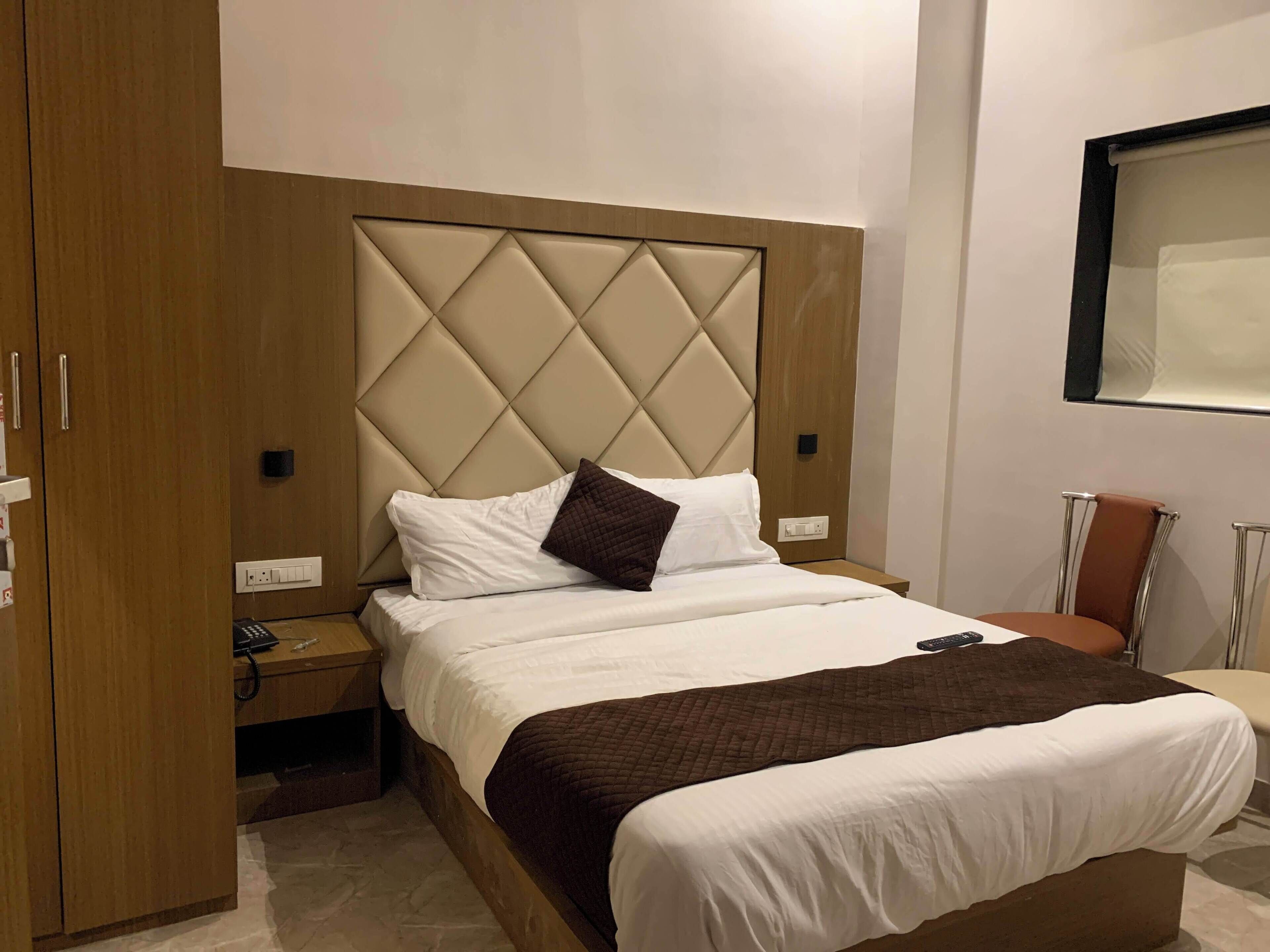 Een hotelkamer met een bed, een nachtkastje, een houten garderobe en een spiegel aan de muur.