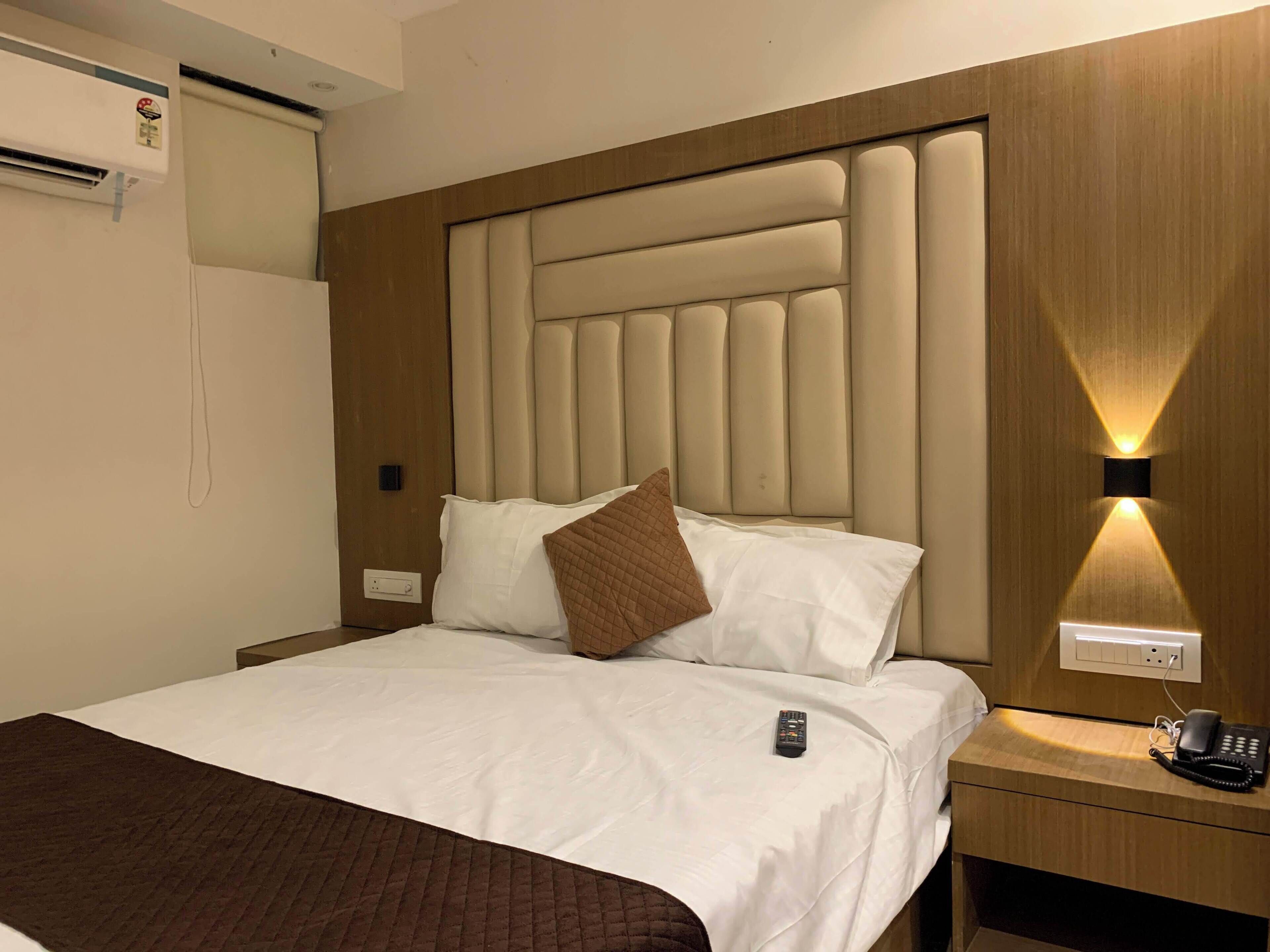 A hotel room with a large bed, a headboard with vertical panels, a bedside table with a phone, and a wall-mounted light.