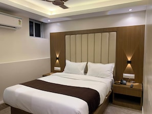A hotel room with a large bed, wooden headboard, bedside lamps, a ceiling fan, and an air conditioning unit.