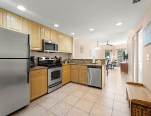 A kitchen with wooden cabinets, stainless steel appliances, and a tiled floor. - Crystal Palms 207 | Modern + Resort Amenities (Treasure Island)