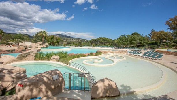 A swimming pool with rock formations, lounge chairs, and a clear sky. - Air-conditioned Apartment with Pool and Tennis in Les Restanques, Grimaud (Grimaud)