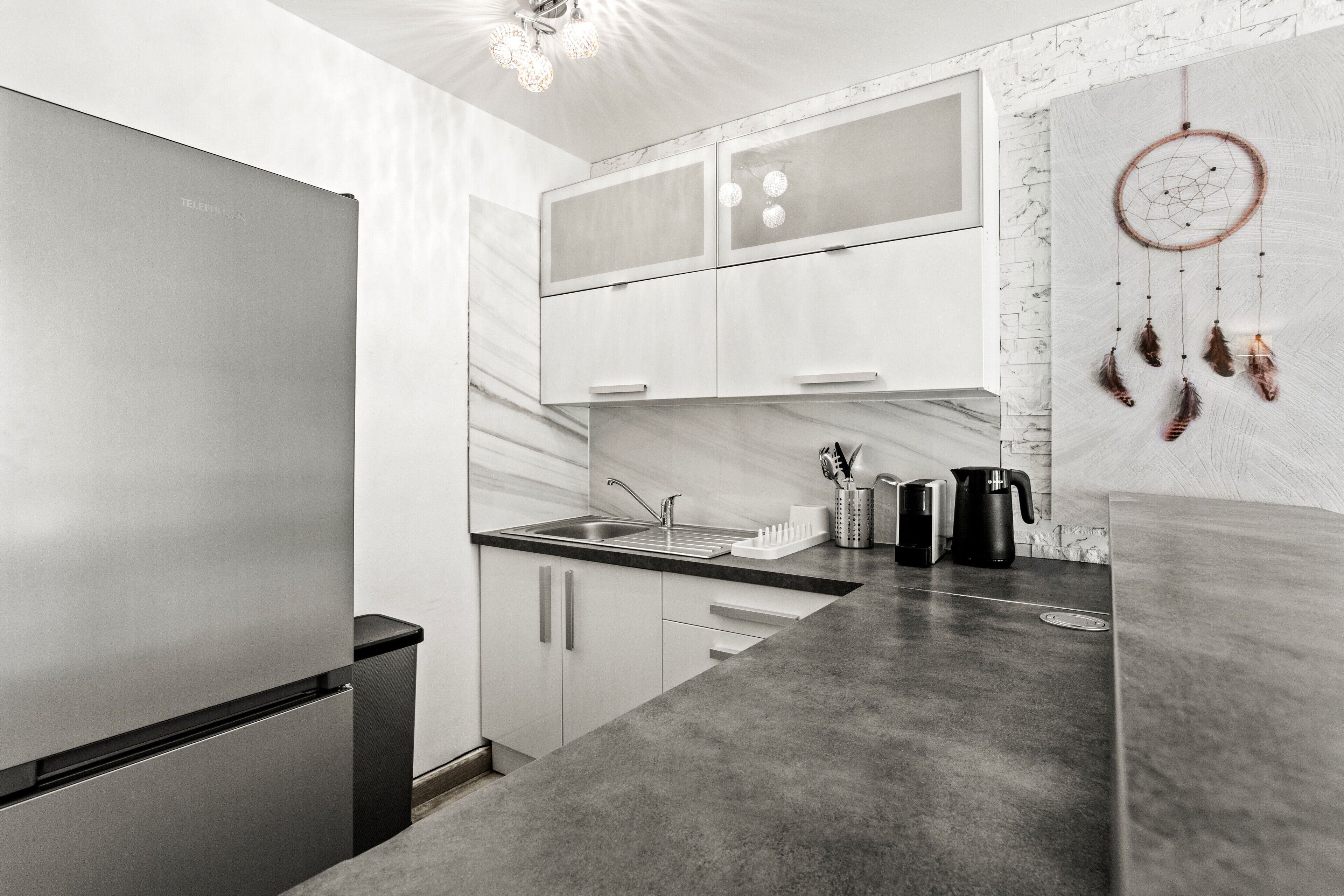 A modern kitchen with a stainless steel refrigerator, a sink, and a dreamcatcher on the wall.