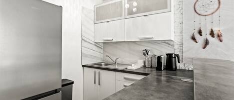 A modern kitchen with a stainless steel refrigerator, a sink, and a dreamcatcher on the wall.