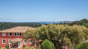 A red villa with a tiled roof, a covered porch, and a view of the sea and hills. - Air-conditioned Apartment with Pool and Tennis in Les Restanques, Grimaud (Grimaud)