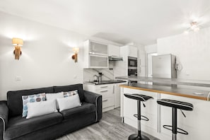 Une cuisine moderne avec des meubles blancs, un canapé noir et deux tabourets de bar.