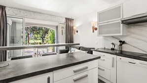 A modern kitchen with a large island, white cabinetry, and a view of greenery outside. - Air-conditioned Apartment with Pool and Tennis in Les Restanques, Grimaud (Grimaud)