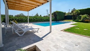 A covered outdoor area with a pool, lounge chairs, and a well-maintained lawn. - Poolside Paradise Dilesi by ΜΡS (Πλάκα Δήλεσι)